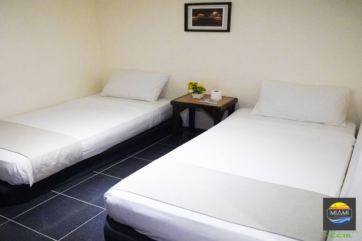 A hotel room with two single beds, a small table with a plant, and a framed picture on the wall.