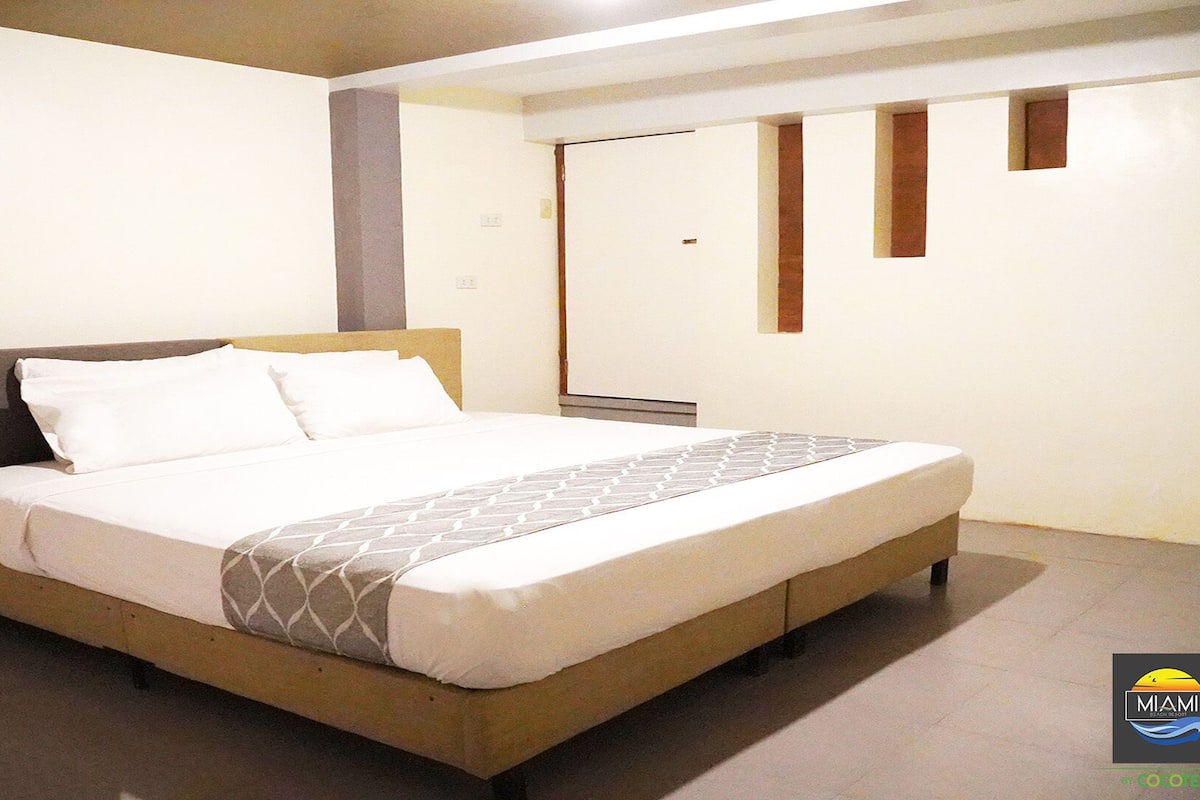 A hotel room with a bed, a bedside table, a mirror, and a wall-mounted TV.