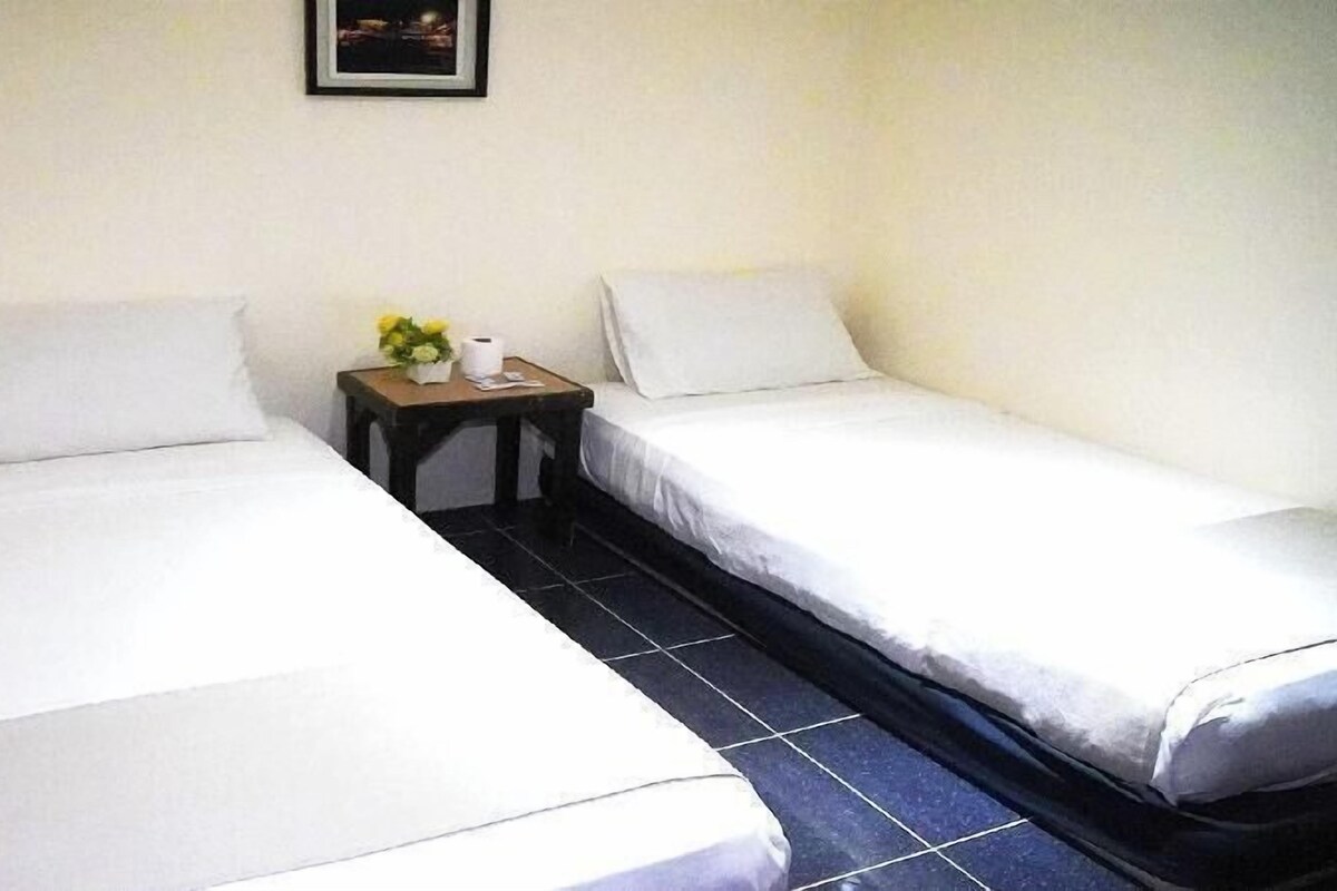 A room with two single beds, a small table with a vase of flowers, and a framed picture on the wall.