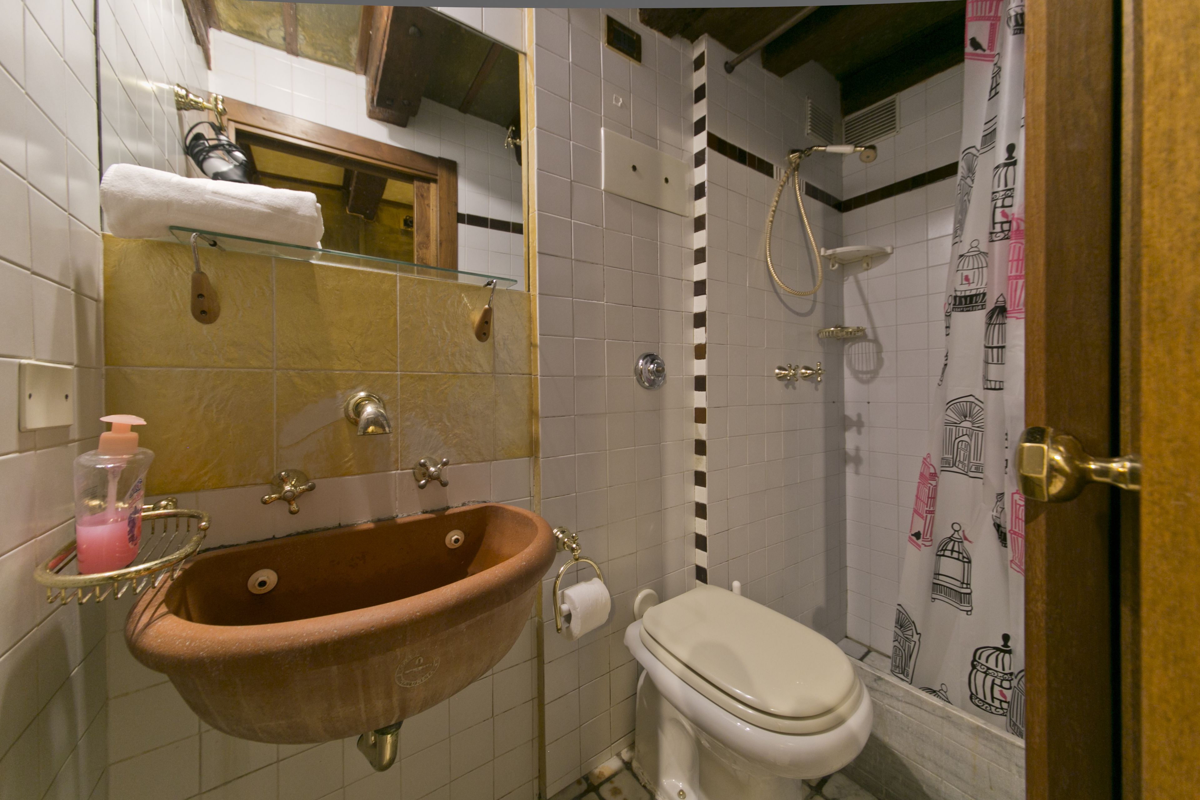 Un baño con lavamanos marrón, inodoro blanco y ducha con cortina estampada.