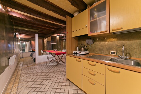 A kitchen with yellow cabinets, a red table, and a tiled floor.