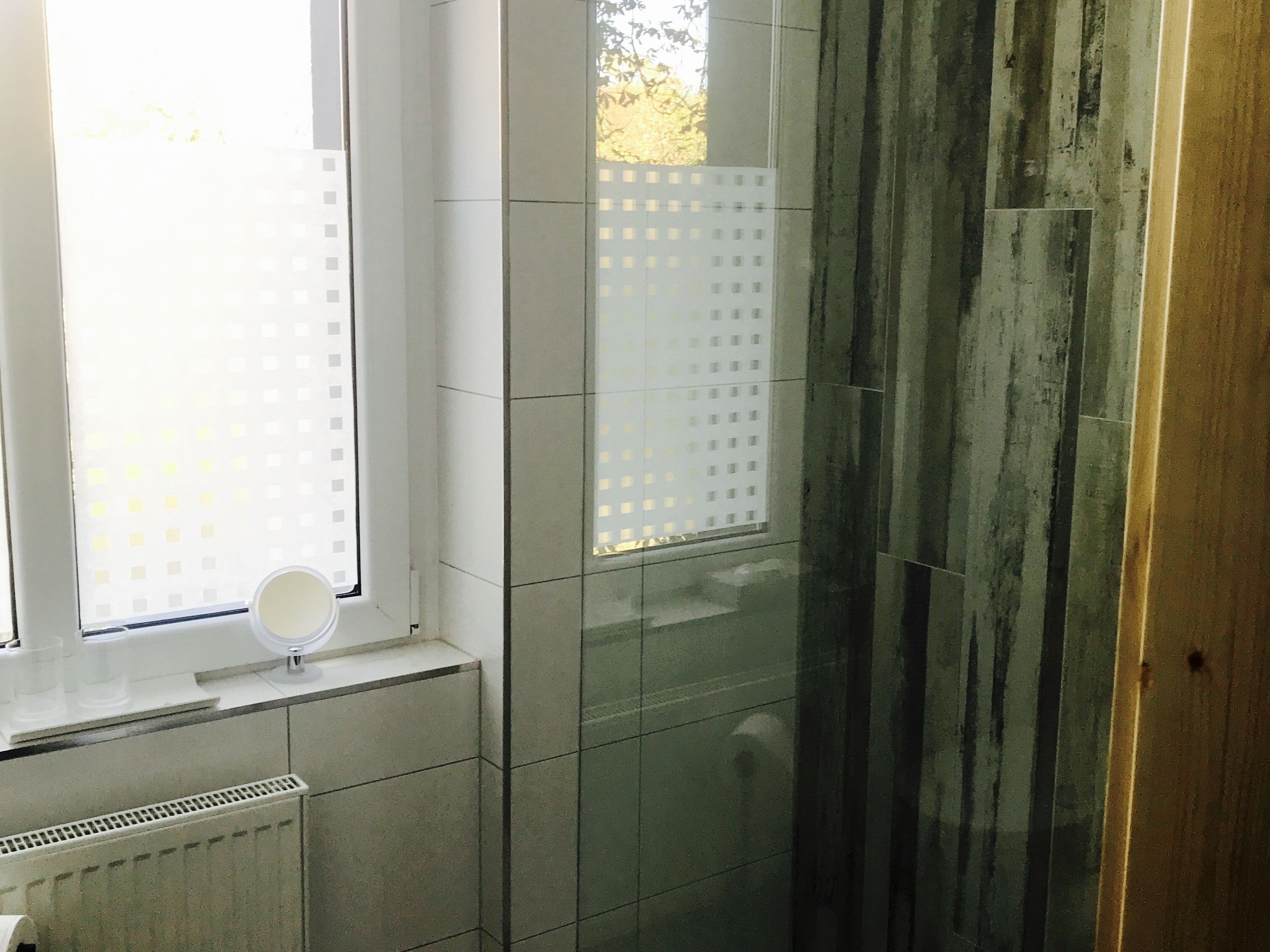 Een badkamer met een raam, een spiegel en een betegelde muur.
