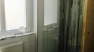 Een badkamer met een raam, een spiegel en een betegelde muur.