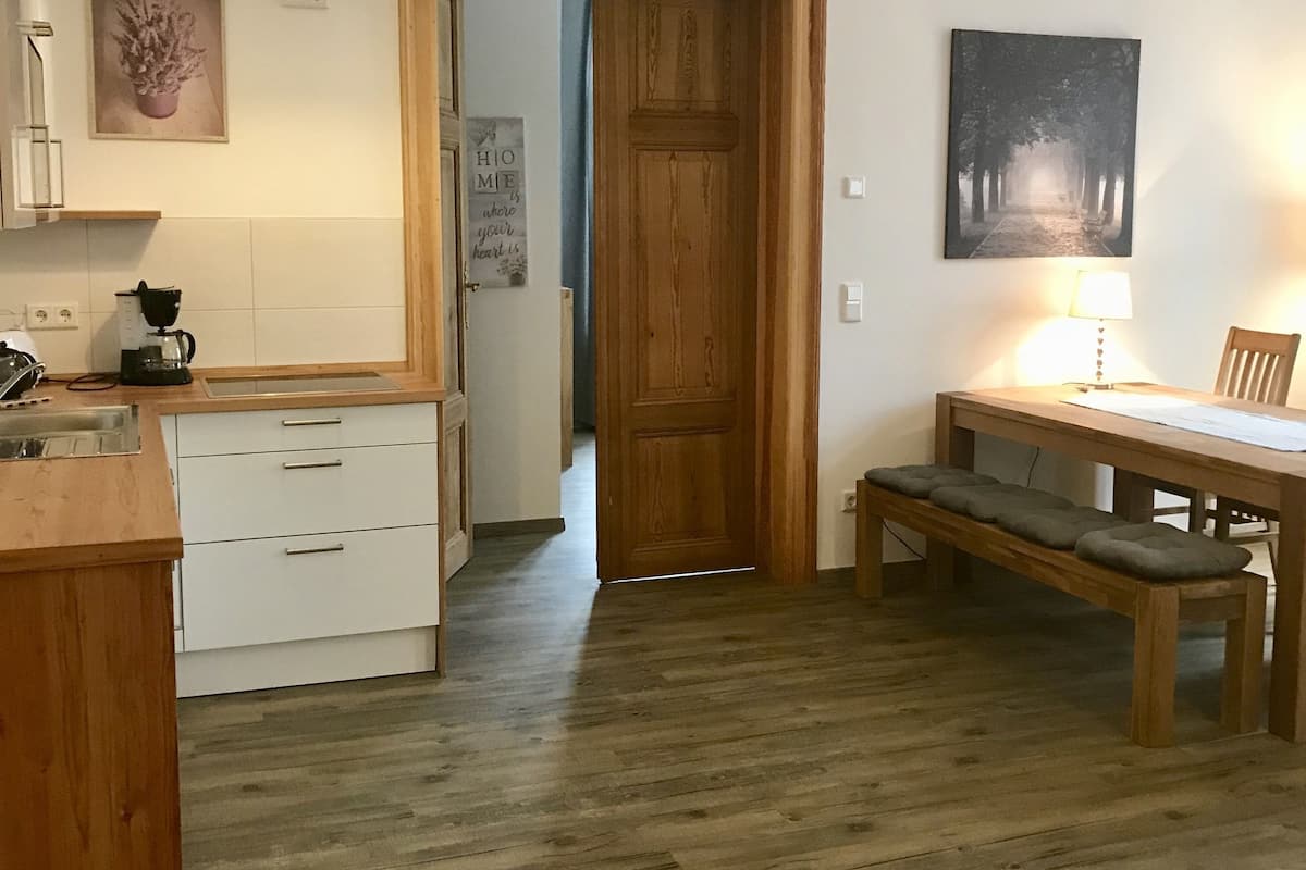 A kitchen with wooden cabinets, a coffee maker, and a dining area with a table and bench.
