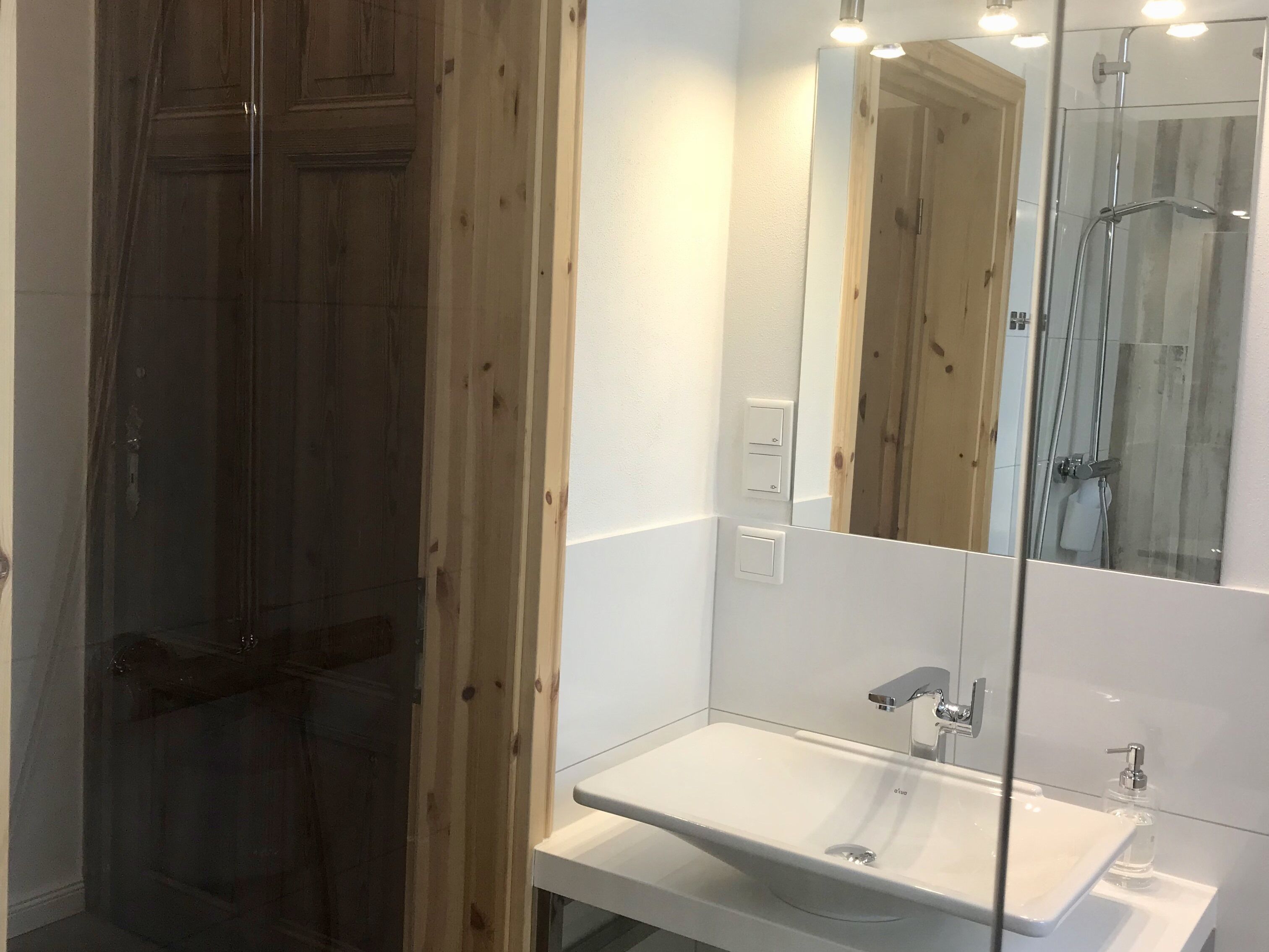 A bathroom with a wooden door, a white sink, a mirror, and a shower.