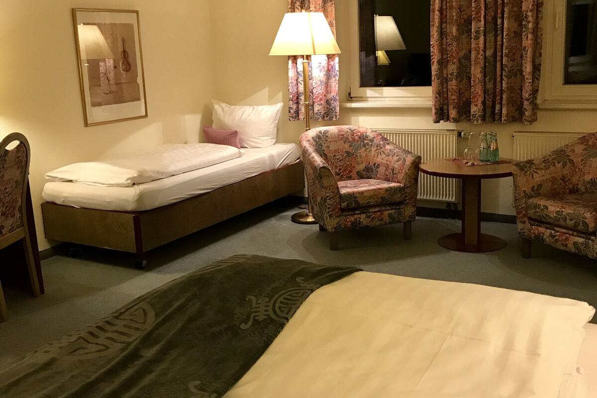 A hotel room with a bed, a small sofa, a chair, a table, and a window with curtains.