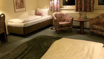 Una habitación de hotel con una cama, un pequeño sofá, una silla, una mesa y una ventana con cortinas.