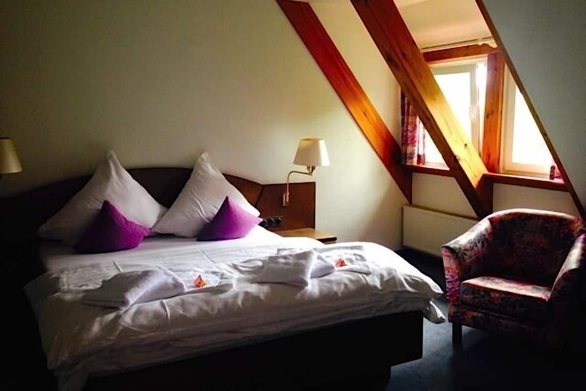A hotel room with a bed, pillows, a chair, a nightstand, and a lamp.