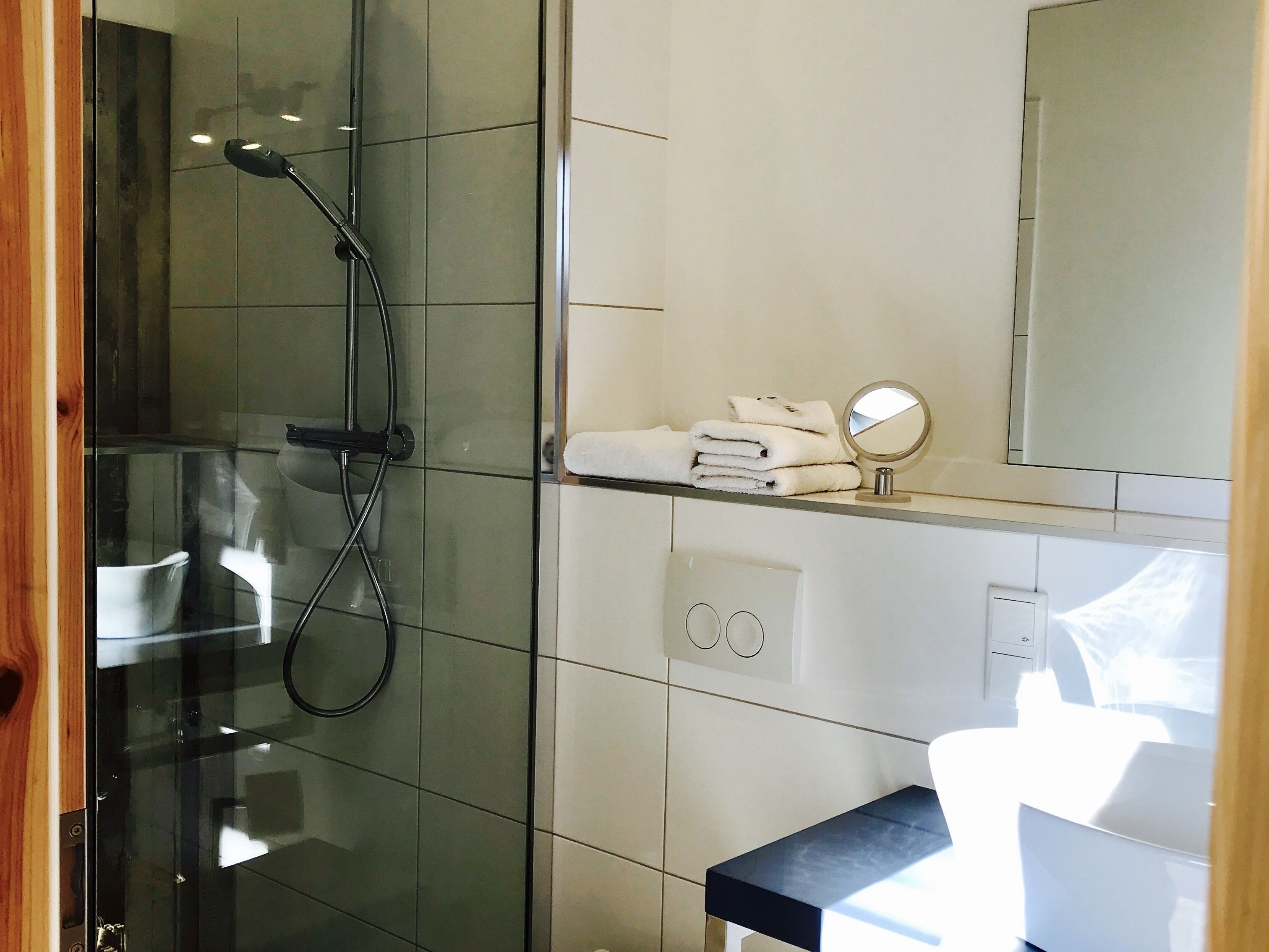 Un baño moderno con cabina de ducha de vidrio, un lavabo blanco y encimera negra, y un espejo sobre el lavabo.