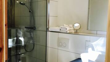 Un baño moderno con cabina de ducha de vidrio, un lavabo blanco y encimera negra, y un espejo sobre el lavabo.