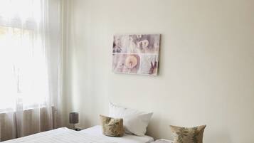 A double bed with white linens, two pillows, a bedside table, and a wall-mounted artwork.