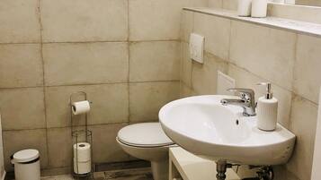 Un baño con lavamanos, inodoro y cubo de basura blancos.