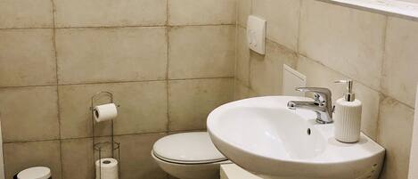 A bathroom with a white sink, toilet, and trash can.