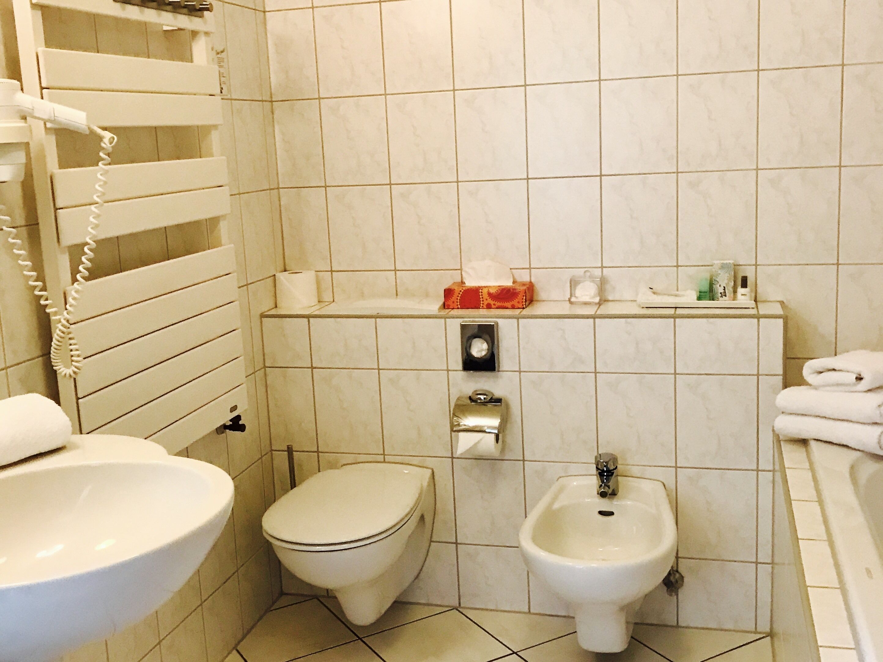 Un baño con inodoro, bidé, lavamanos y toallero.