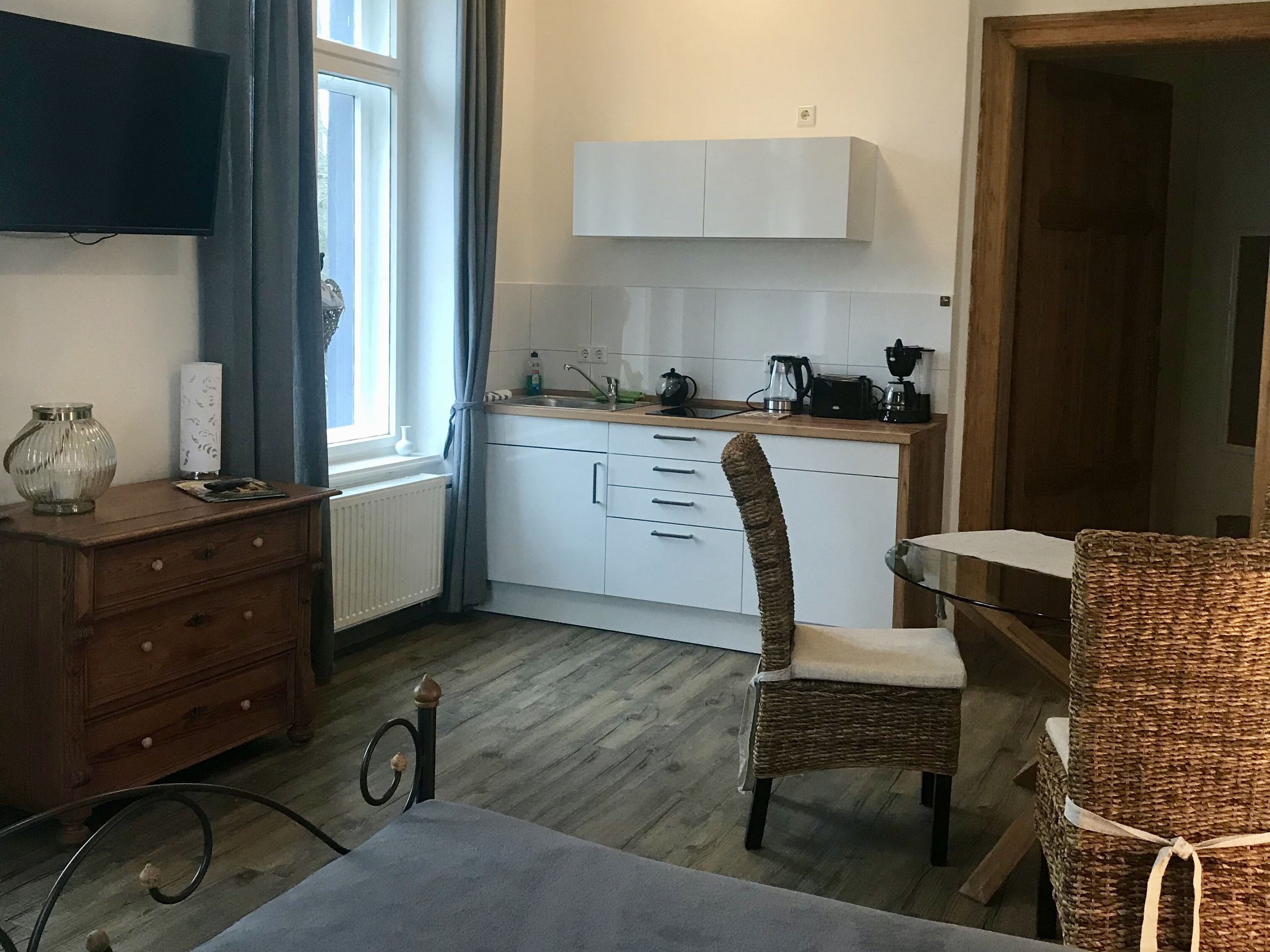 A compact kitchen with white cabinets, a wooden countertop, and a wicker chair.