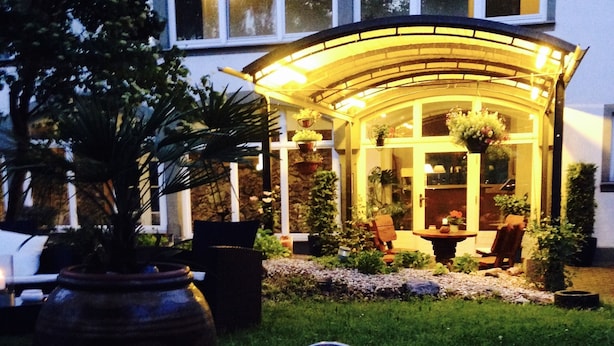 A well-lit outdoor area with a covered seating area, potted plants, and a large metal container. - Hotel Dein Gutshof (Görlitz)