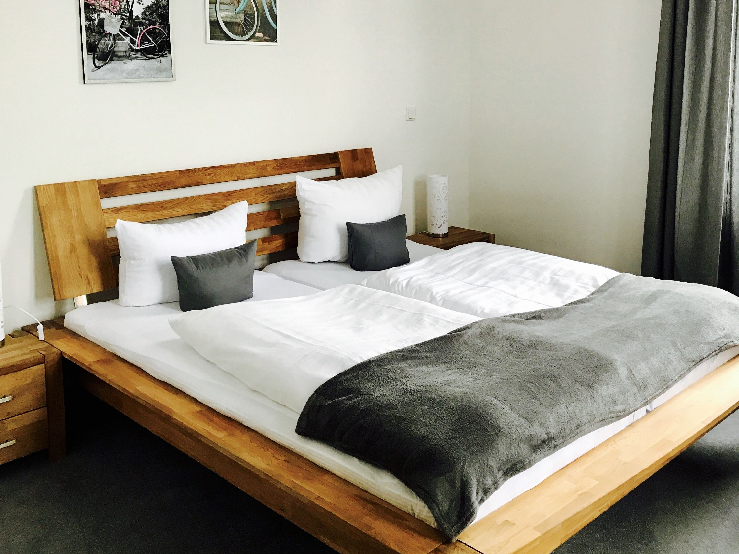 Ein Doppelbett mit Holz Kopfteil, weißer Bettwäsche und einer grauen Tagesdecke. Zwei Nachttische mit Lampen und ein kleiner Beistelltisch mit einer Lampe.