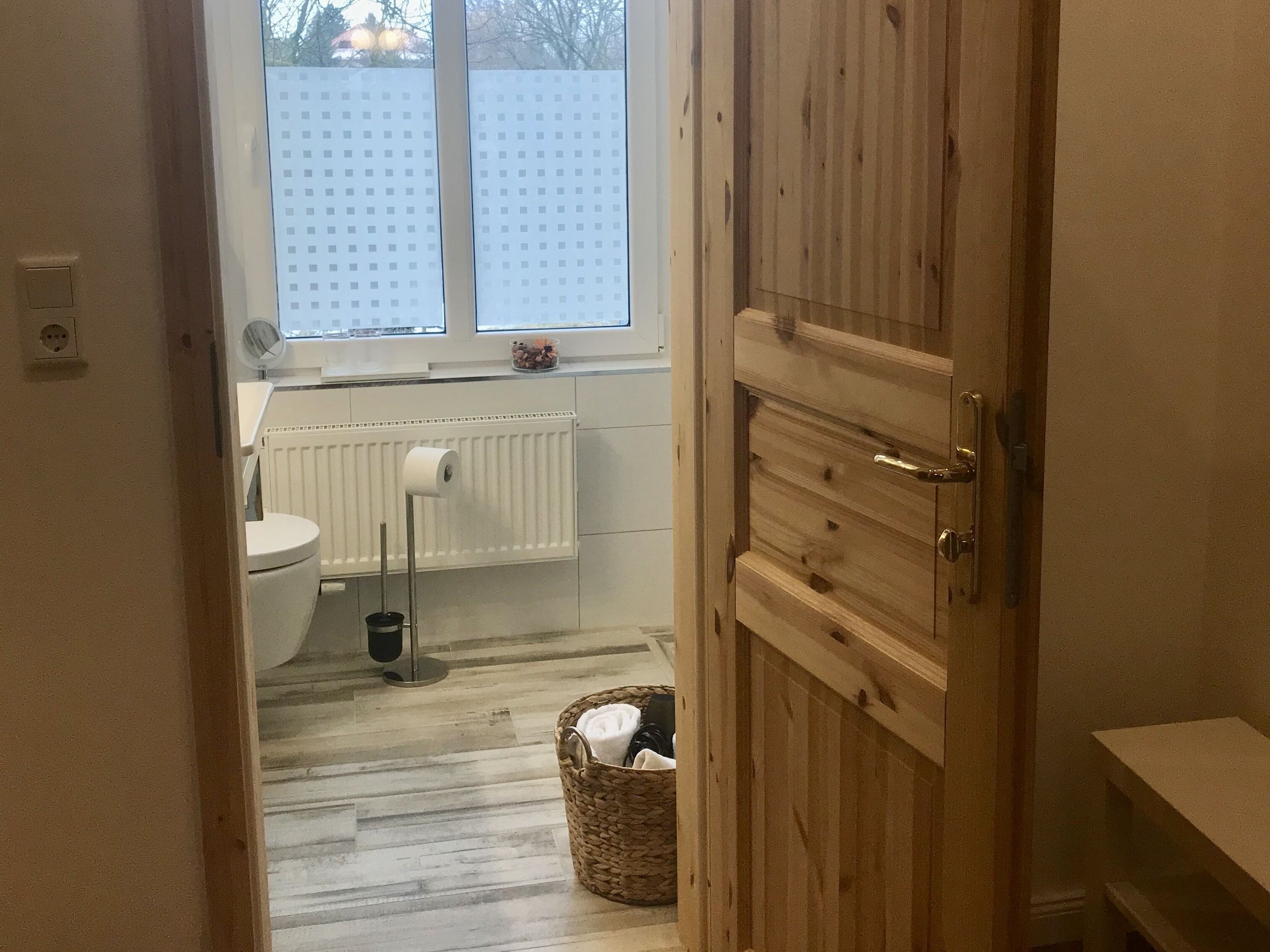 A bathroom with a toilet, a radiator, a window, and a wooden door.
