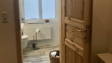 A bathroom with a toilet, a radiator, a window, and a wooden door.