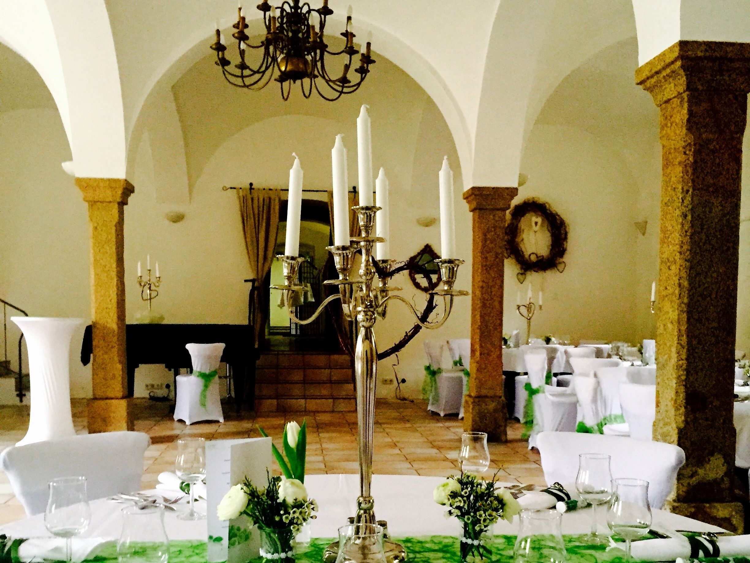 Un gran saló de banquets amb taules preparades per a un esdeveniment formal, amb teles blanques, centrals florals i un penjall.