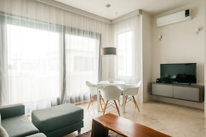 Ein modernes Wohnzimmer mit einer Couch, einem Esstisch, Stühlen, einem Fernseher und einer Klimaanlage.
