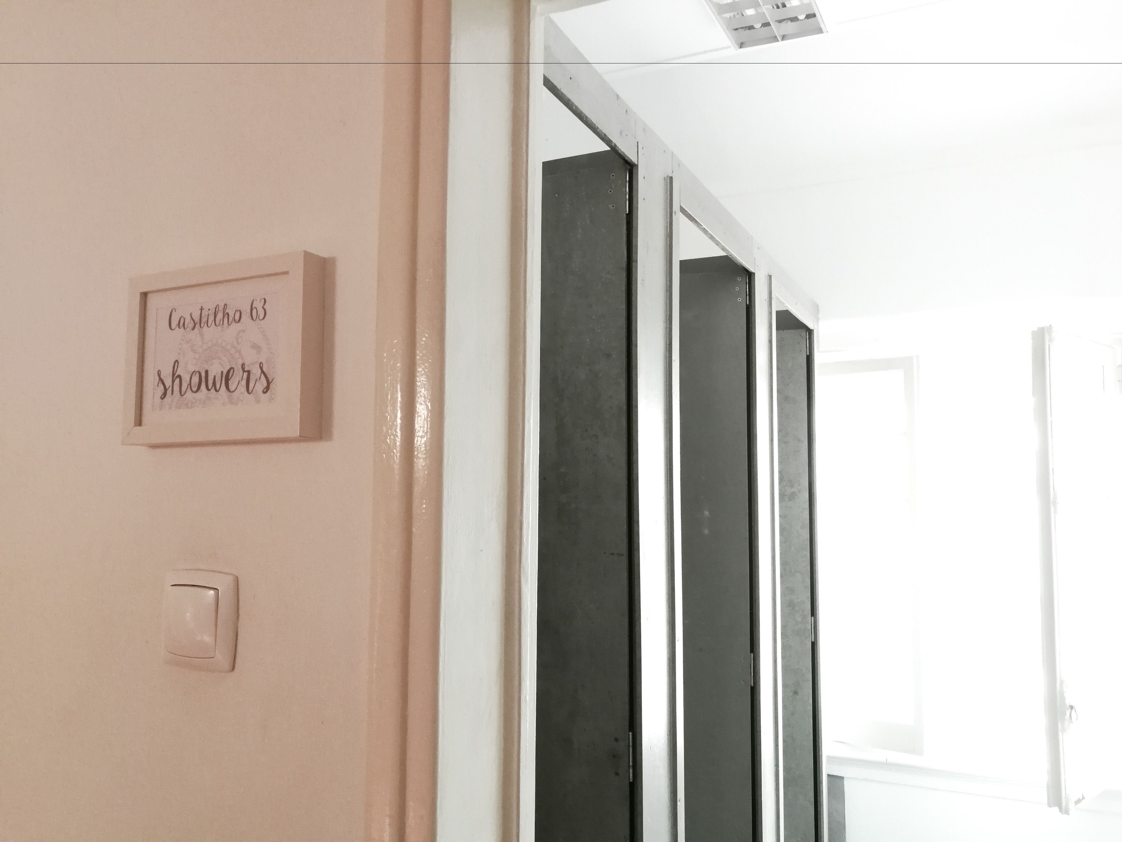 A hallway with a framed sign reading "Castilho 63 showers" and a light switch on the wall.
