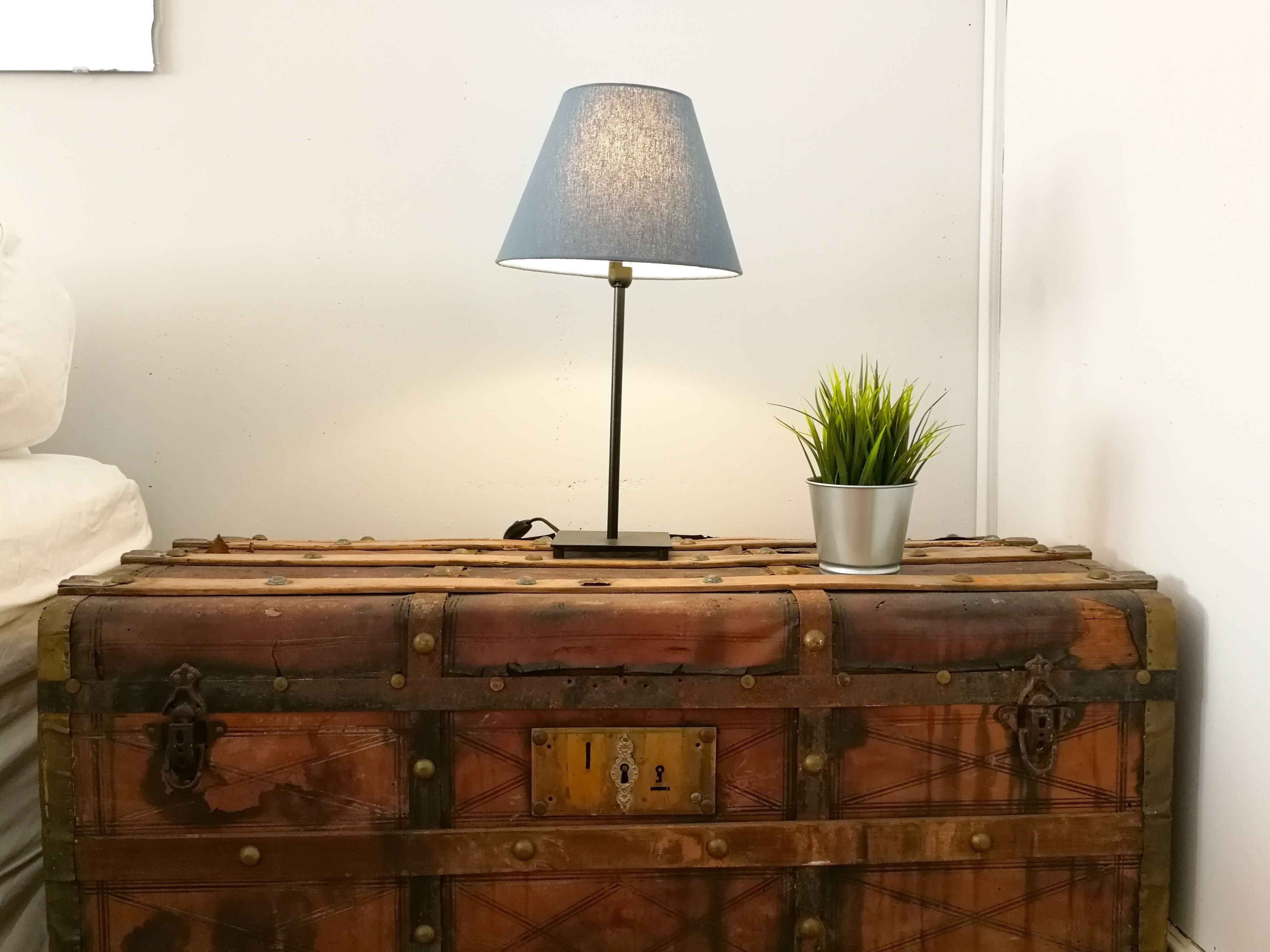 Un coffre en bois rustique, surmonté d’une lampe en métal et d’une petite plante en pot.