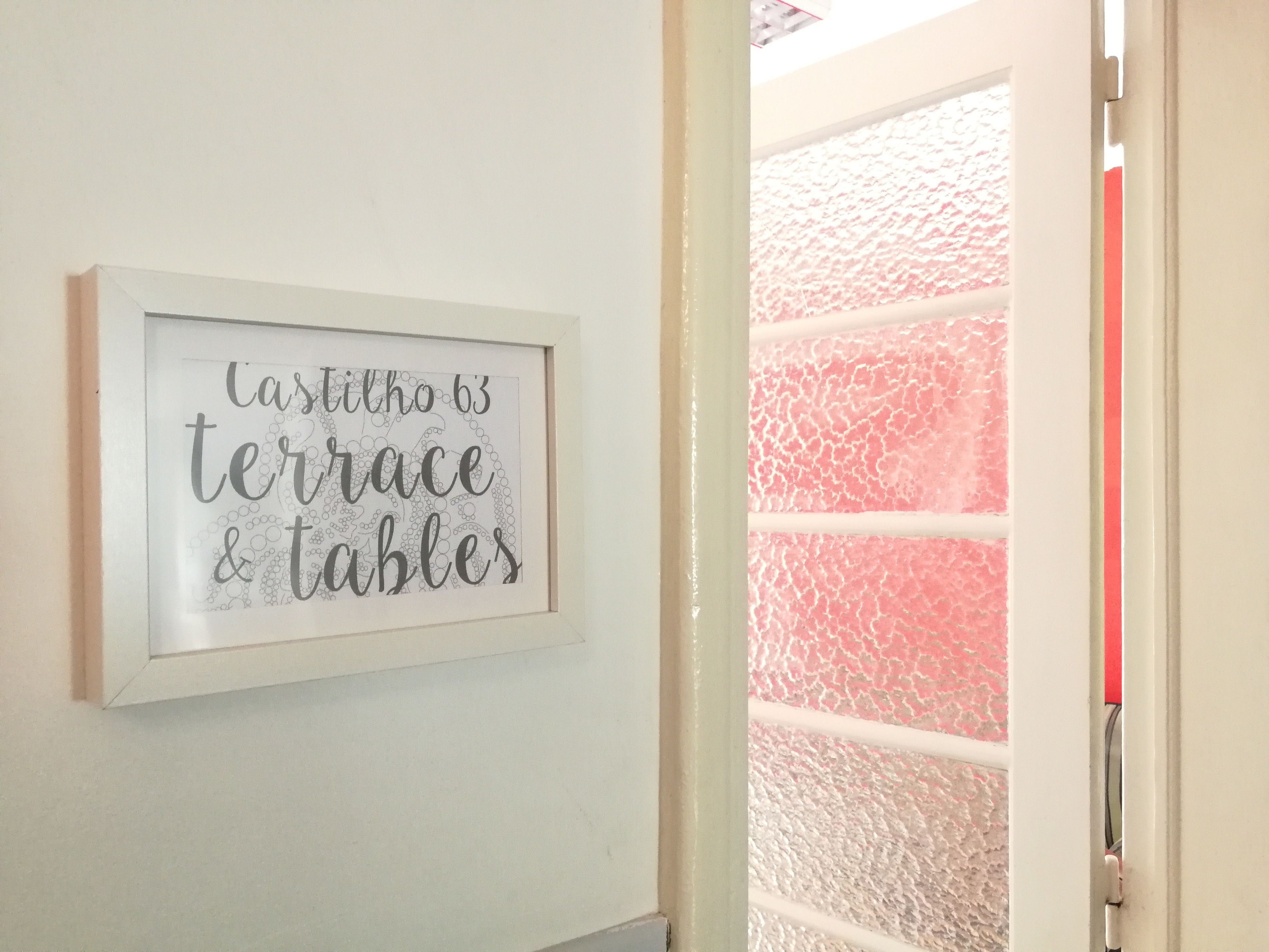 A framed sign with the text "casillho 63 terrace & tables" on a white wall.