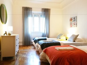 Une chambre avec deux lits, une commode, une fenêtre avec des rideaux et un tableau au mur.