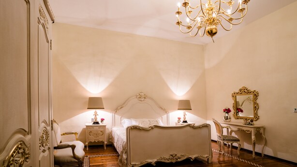Une chambre à coucher avec un grand lit, deux tables de chevet avec des lampes, une coiffeuse avec un miroir et un lustre.