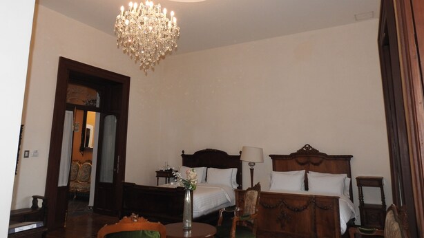 Habitación de hotel con dos camas, un candelabro, un jarrón con flores y una silla de madera.
