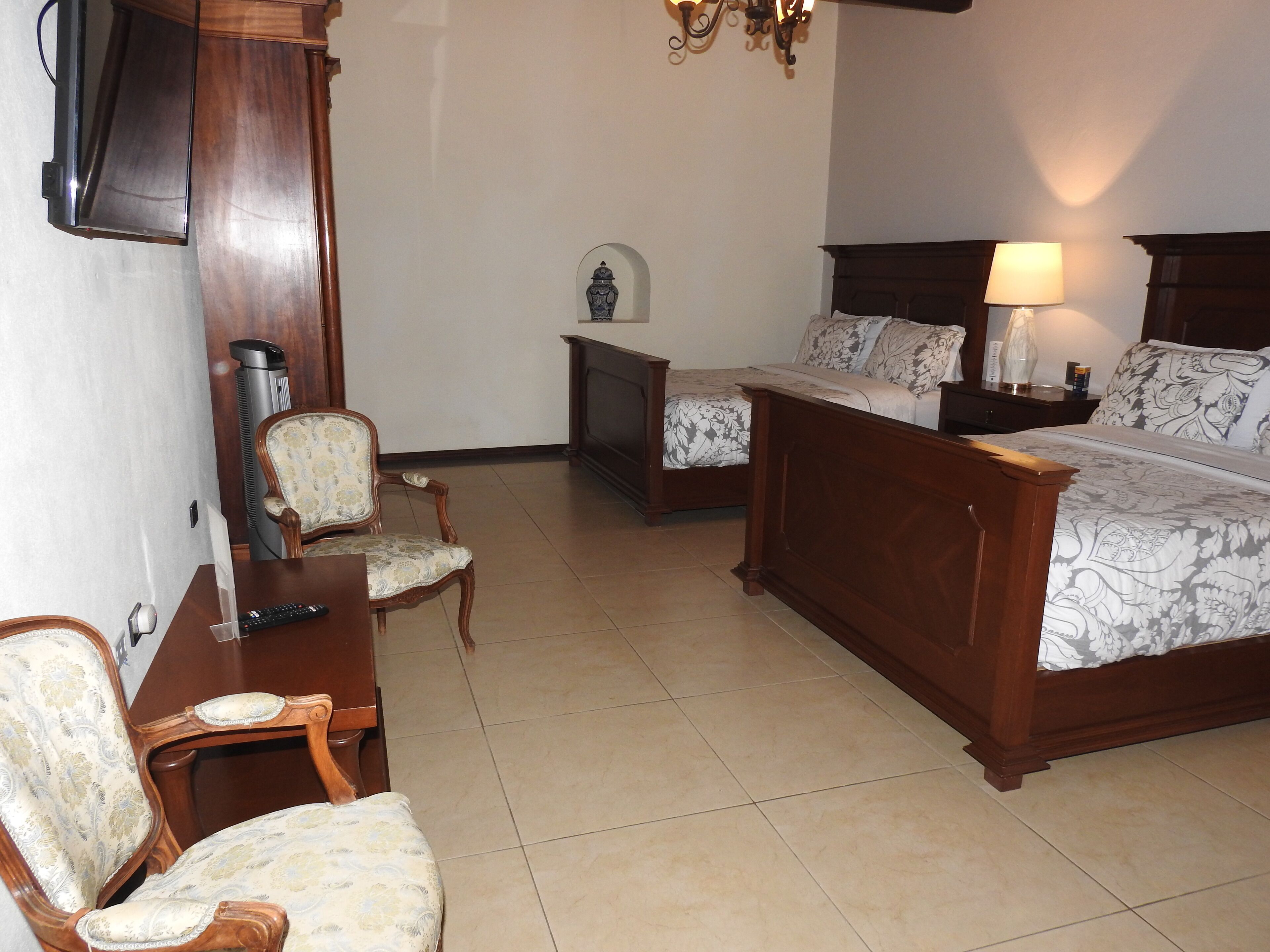 A bedroom with a large bed, two smaller beds, a chair, a nightstand, a lamp, a heater, and a television.