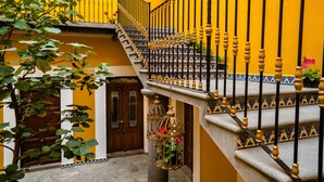 Un escalier orné de balustres noirs et de marches à motifs bleus et blancs, menant à un mur jaune sur lequel se trouve une porte en bois.