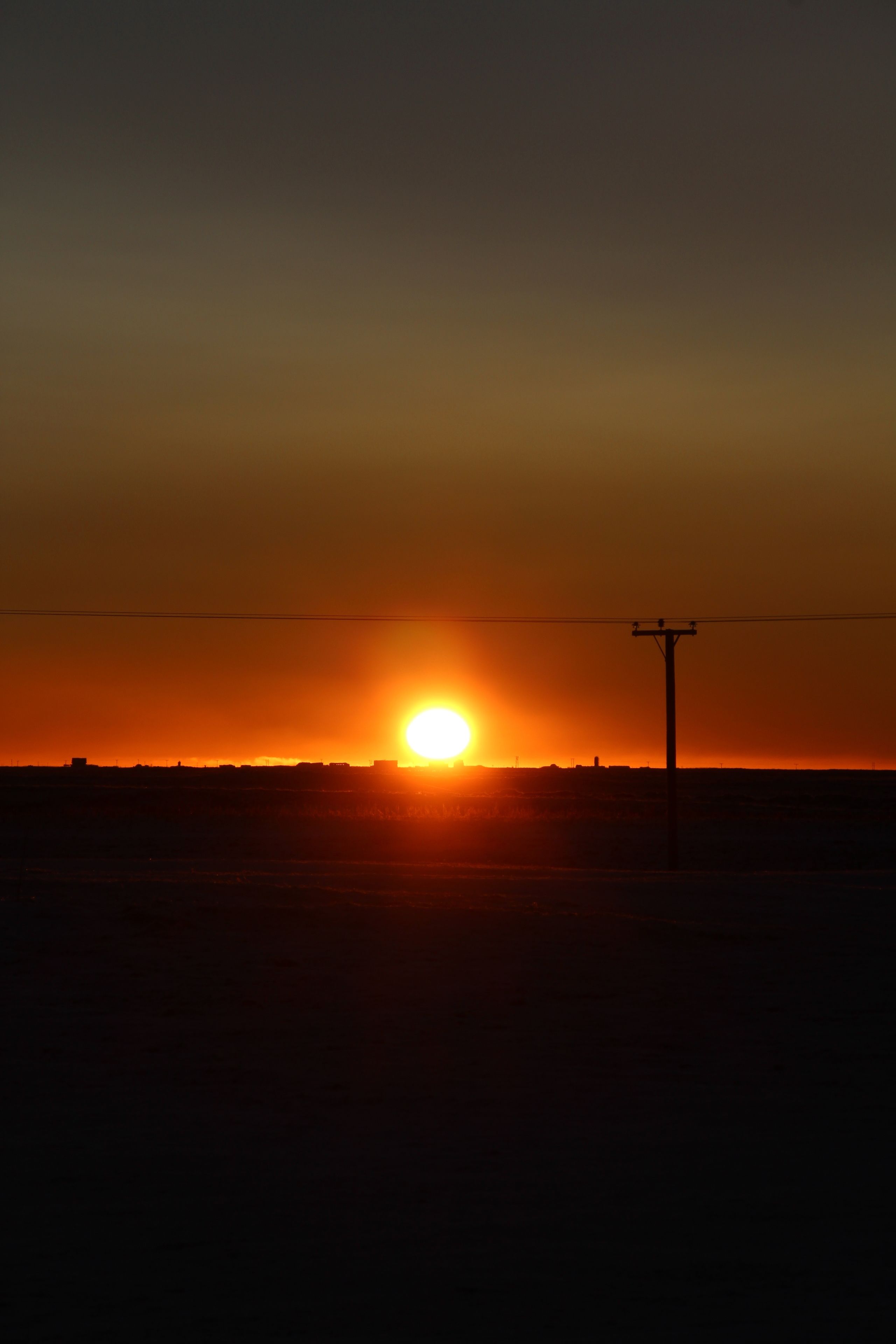 Atardecer sobre una llanura extensa con un poste de electricidad al frente.