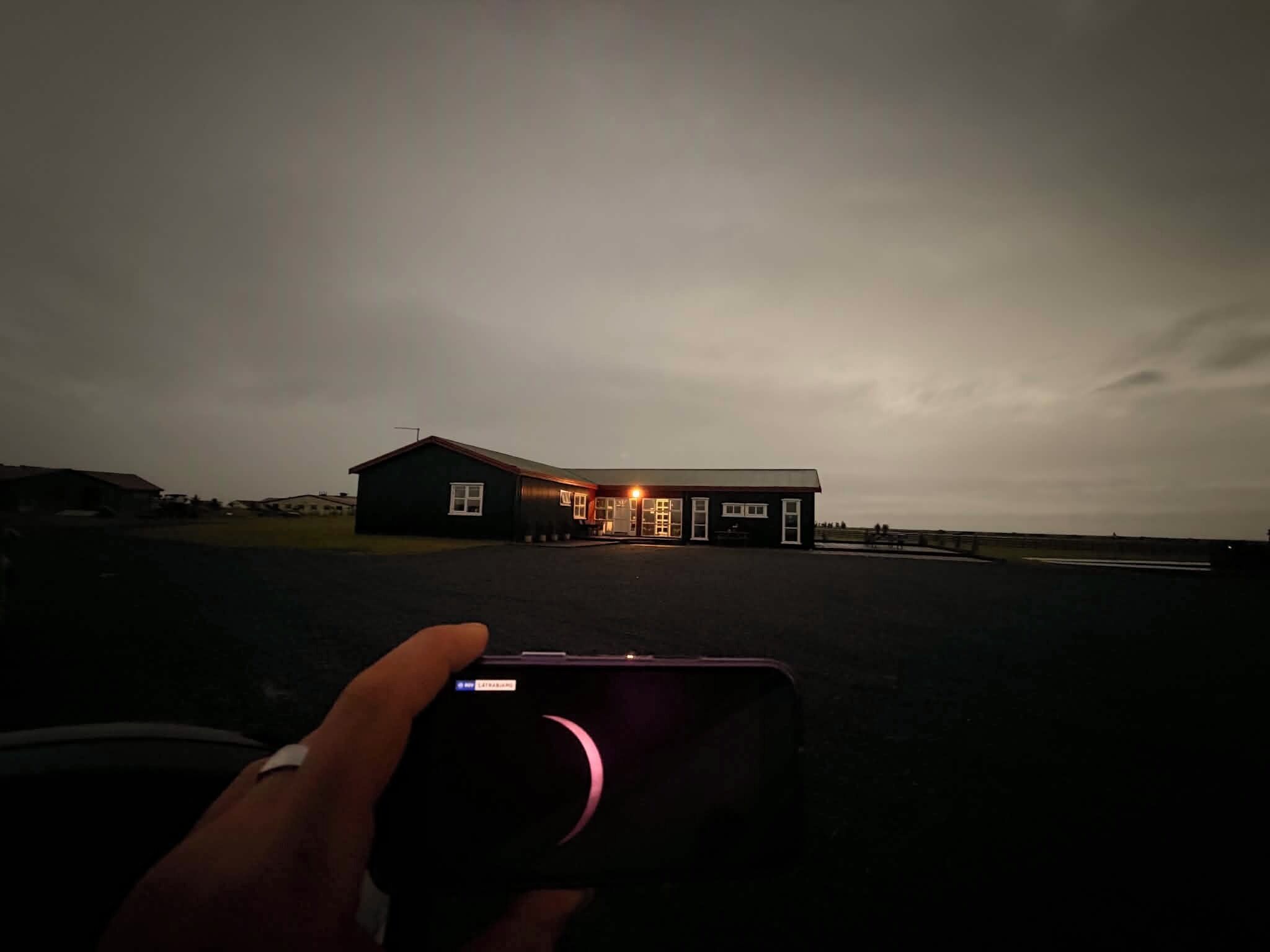 Un edificio con fachada oscura y ventanas iluminadas, ubicado en un terreno plano sin vegetación visible.