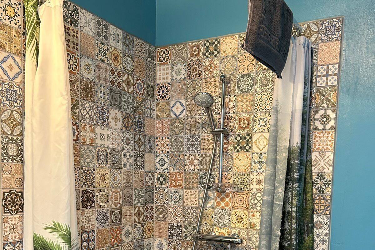 A shower area with a tiled wall featuring a variety of patterns, a handheld showerhead, and a curtain.