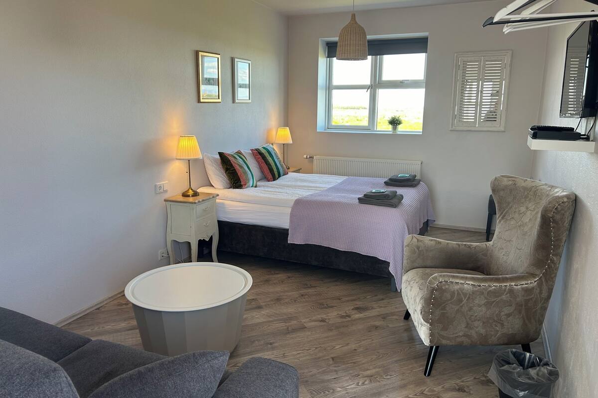 A bedroom with a bed, bedside lamps, a chair, a round table, and a window with blinds.