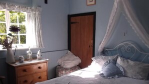 Een slaapkamer met een bed, nachtkastje, dressoir, raam met gordijnen en een deur.