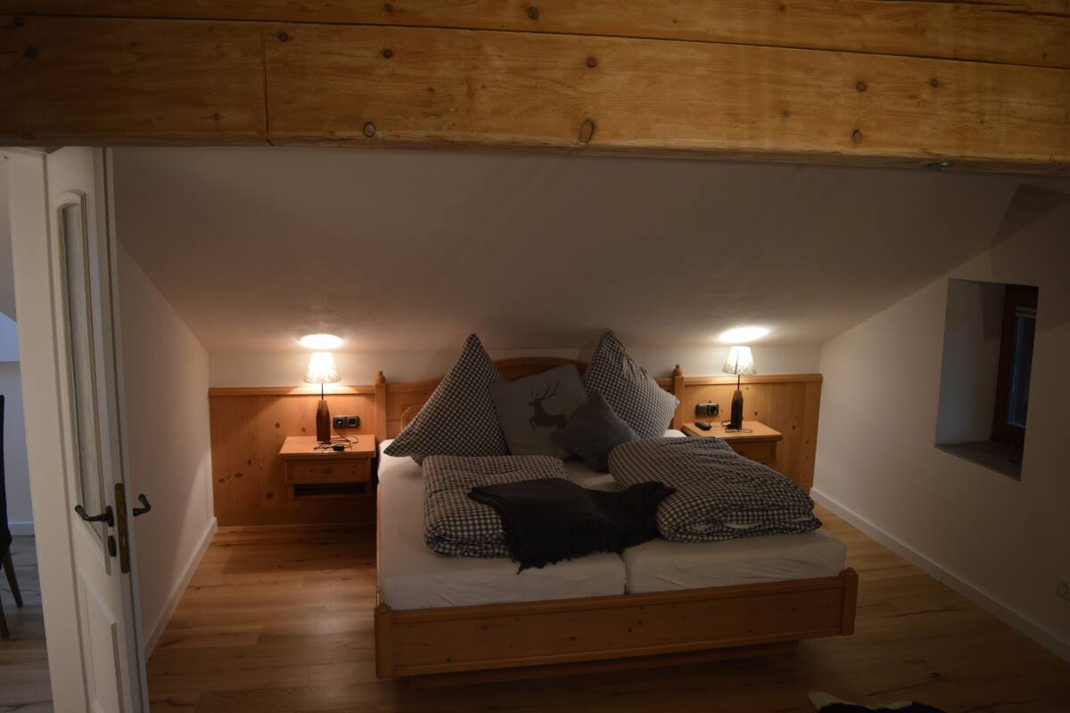 A bedroom with a loft bed, wooden headboard, bedside lamps, and a small window.