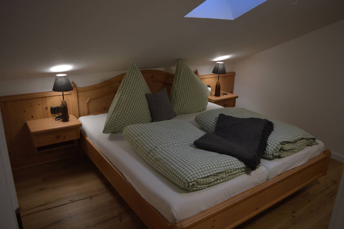 A single bed with a skylight, wooden headboard, bedside tables with lamps, and a checkered bedspread.