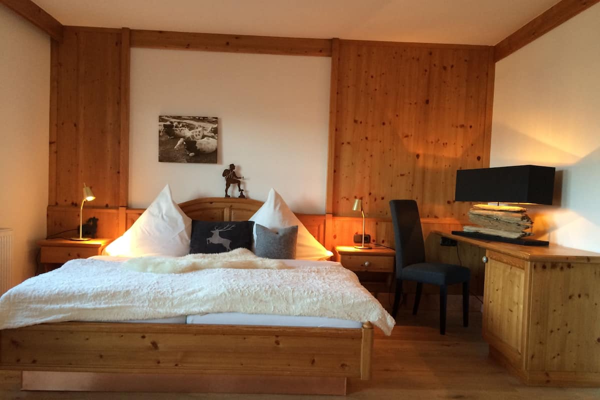 A wooden bedroom with a bed, bedside tables, a desk, and a chair.