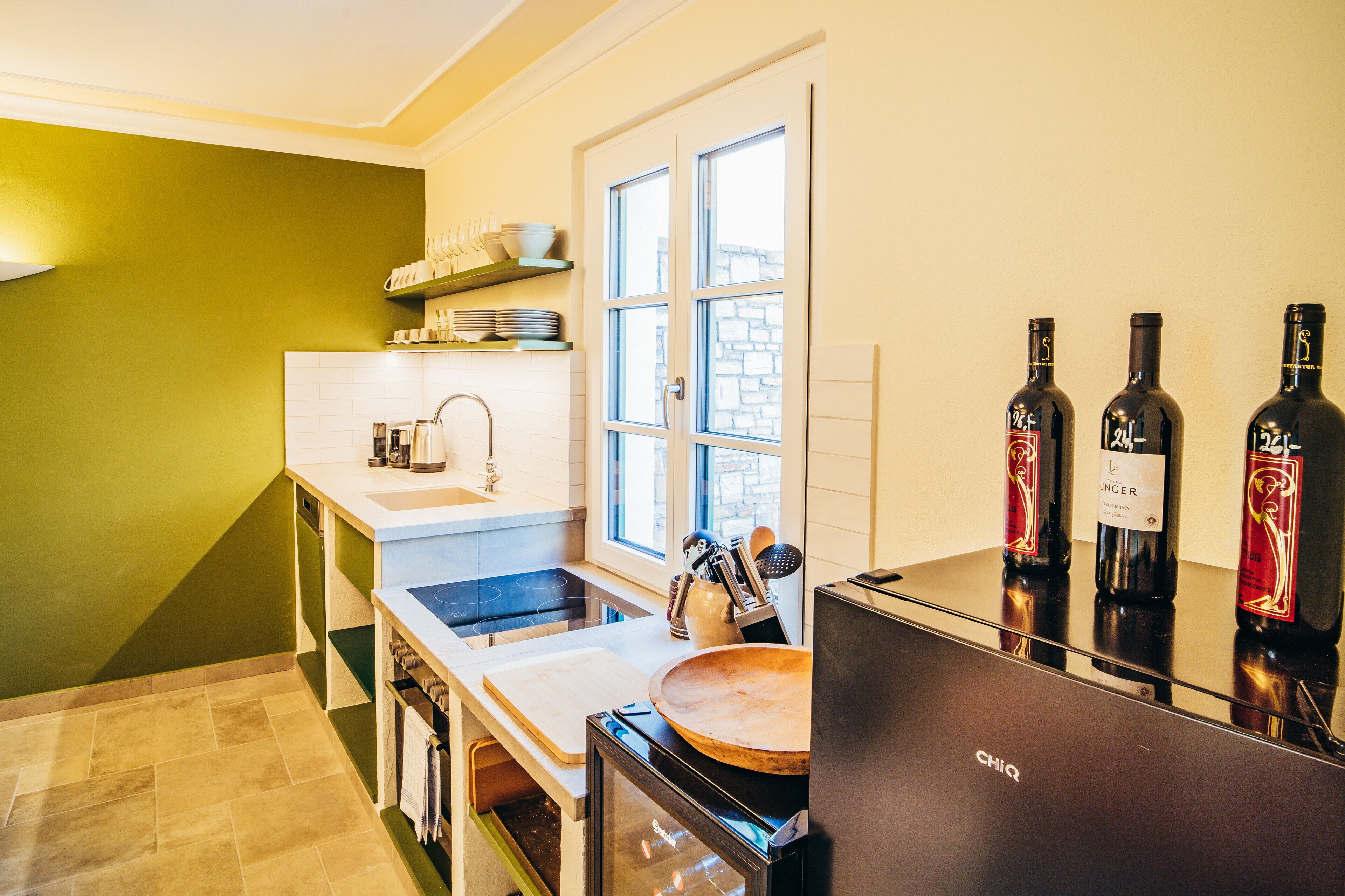 Una cocina moderna con horno empotrado, un fregadero y una ventana. Hay botellas de vino en la encimera.