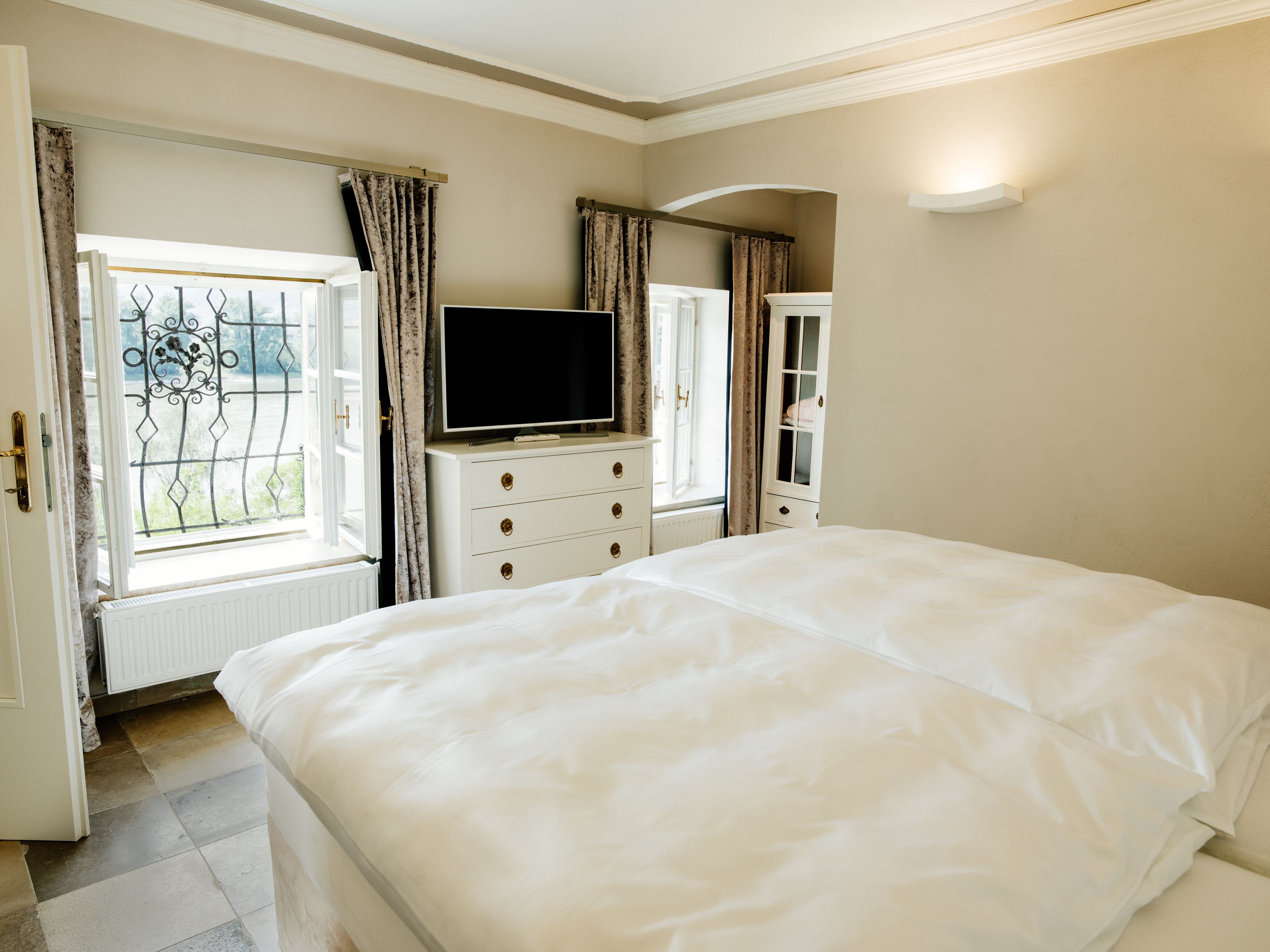 A bedroom with a large bed, a dresser with a TV, and a window with curtains.