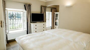 A bedroom with a large bed, a dresser with a TV, and a window with curtains.