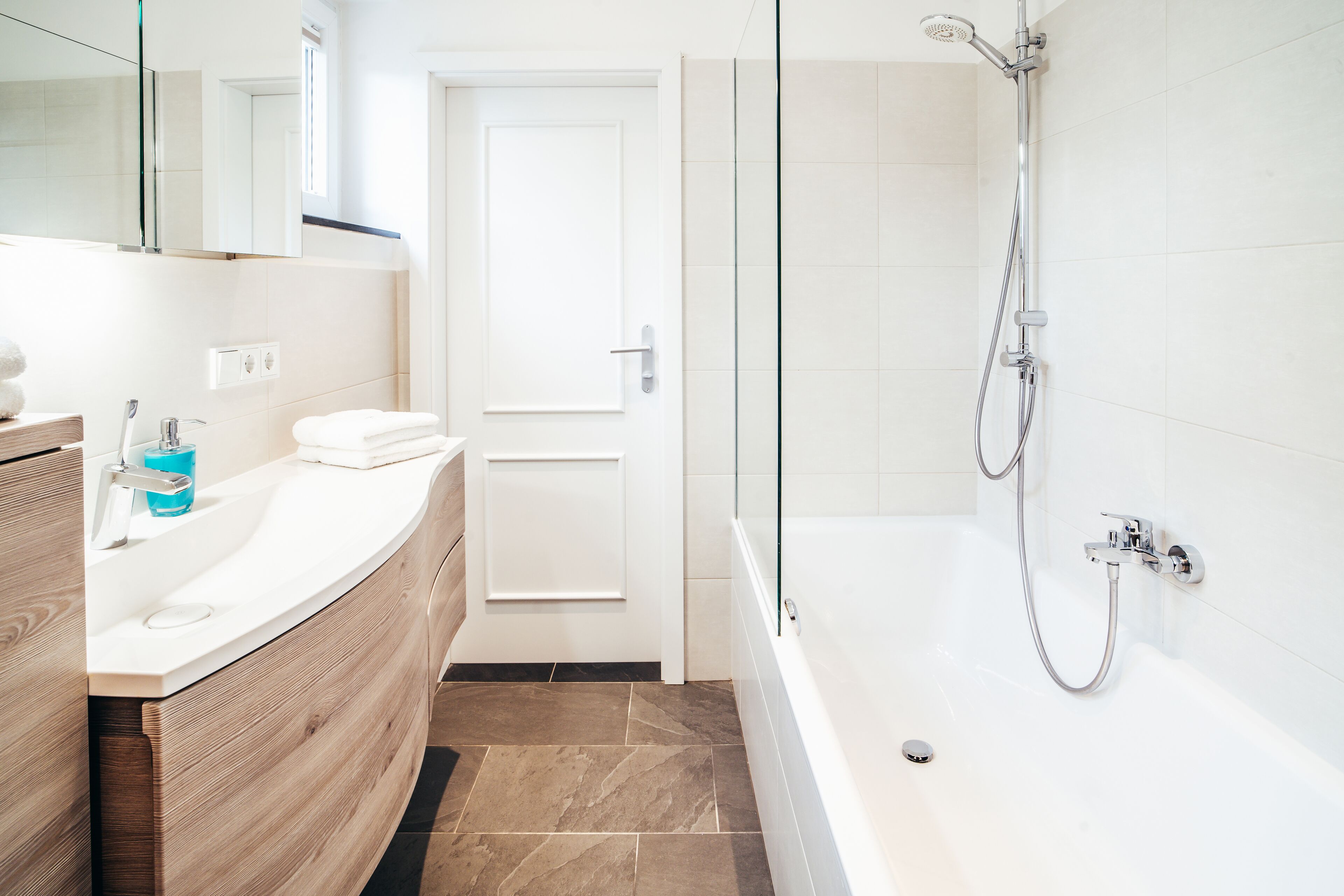 A modern bathroom with a white sink, wooden vanity, and a glass-enclosed shower area.