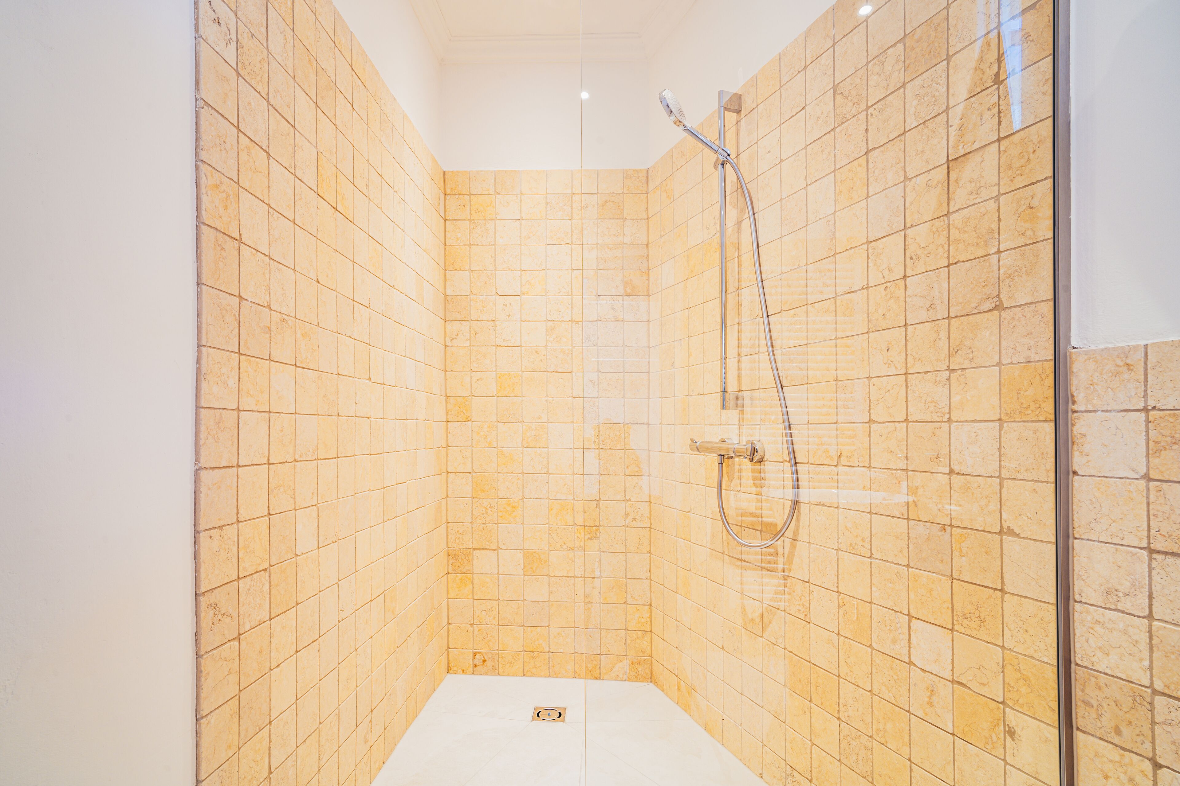 A small, tiled shower room with a handheld showerhead and a wall-mounted faucet.