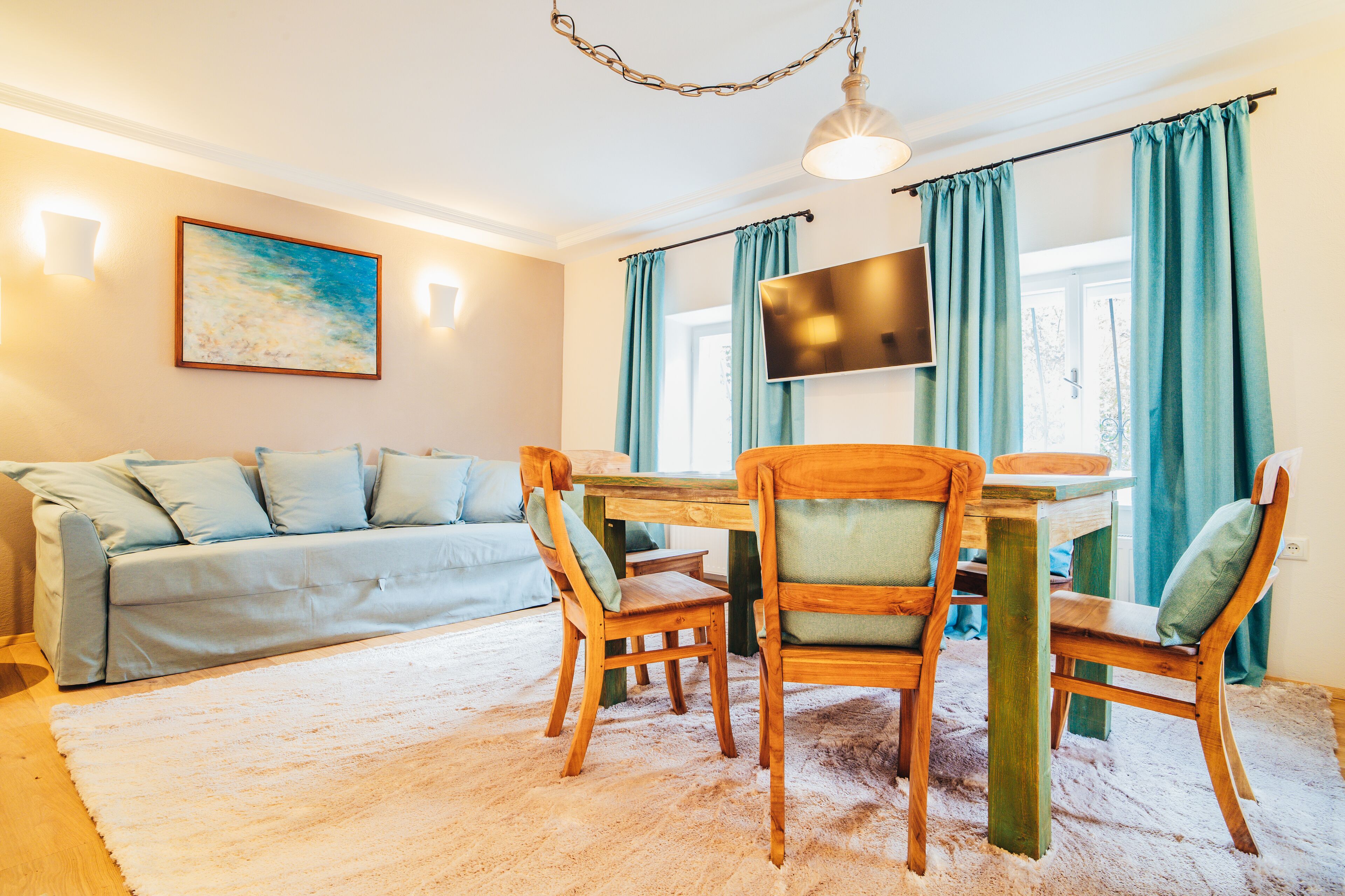 A cozy living room with a sofa, wooden chairs, a TV, and a dining table.