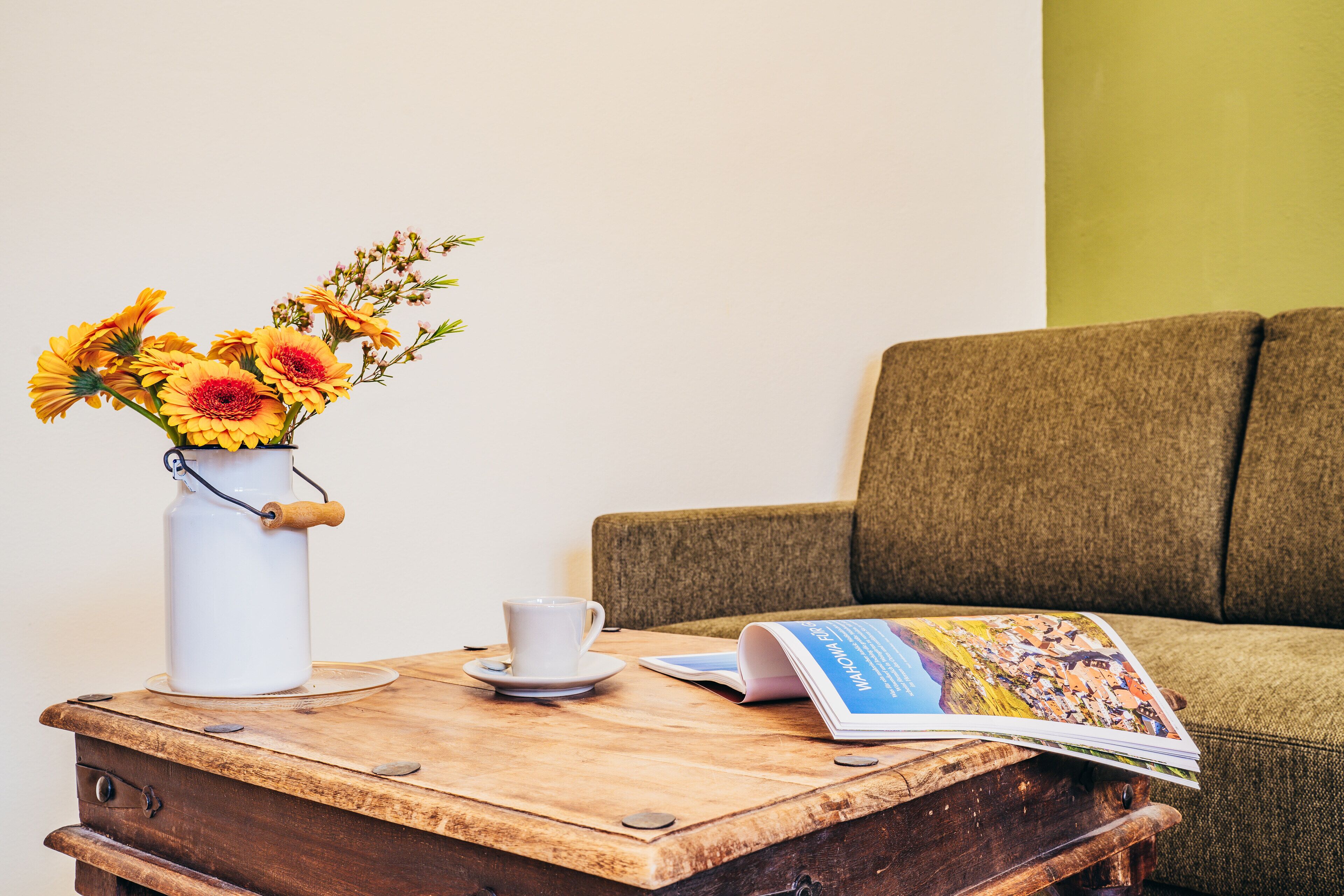 A wooden table with a white vase containing yellow flowers, a white cup, and a magazine.