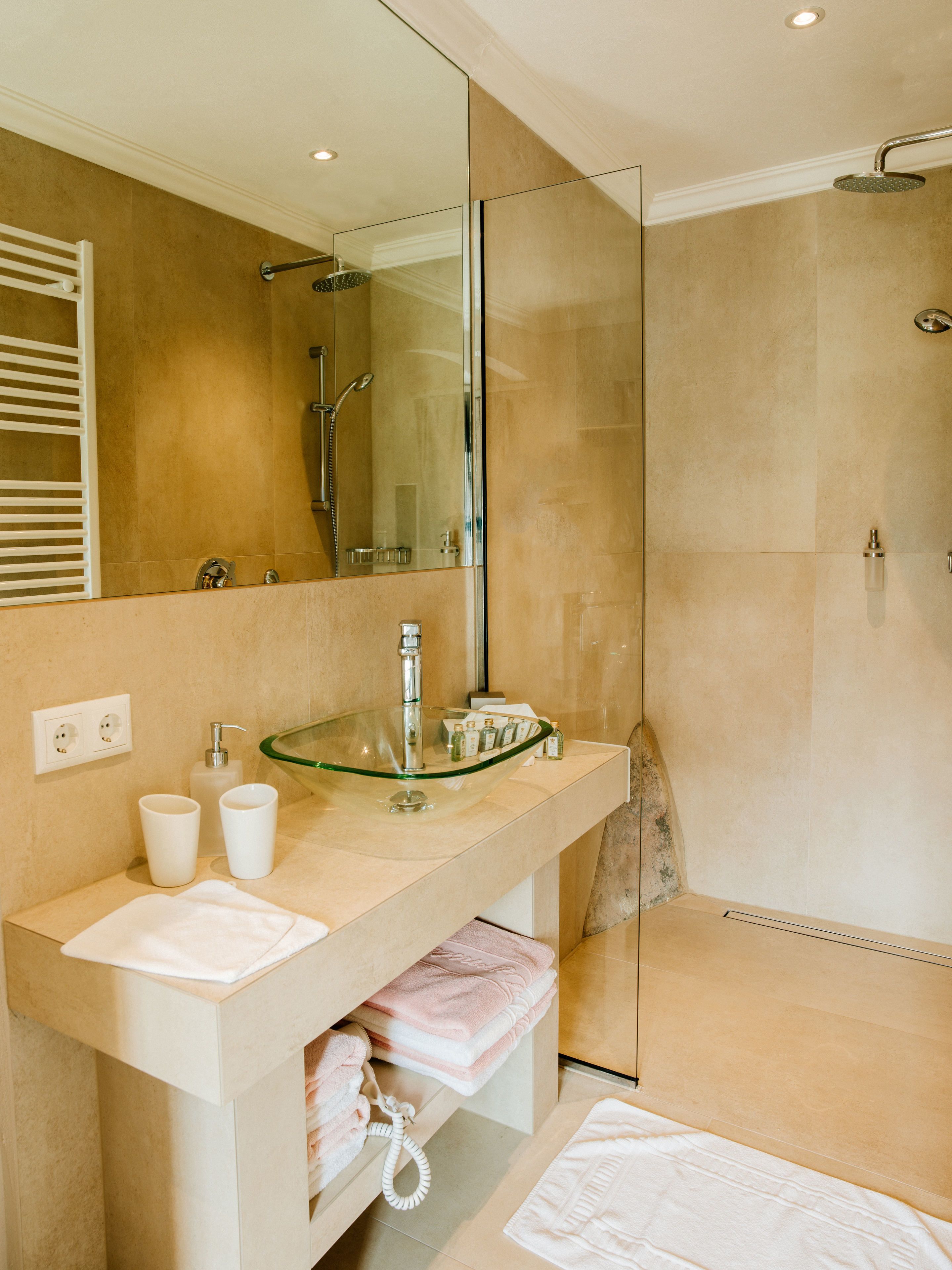 A modern bathroom with a glass sink, a large mirror, and a walk-in shower.