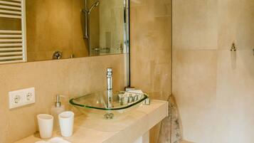 A modern bathroom with a glass sink, a large mirror, and a walk-in shower.